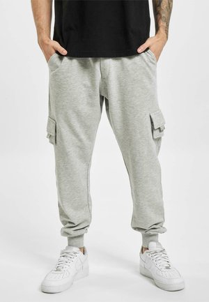 Grå joggebukser laget av myk stoff, med cargo-lommer på siden, ribbestrikkede mansjetter og elastisk midje. Sammen med hvite sneakers.