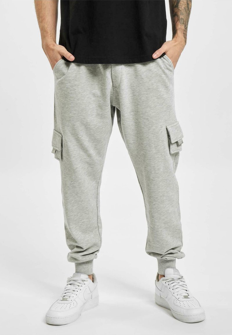 Graue Jogginghose aus weichem Material, mit Cargo-Taschen an den Seiten, gerippten Bündchen und einem elastischen Bund. Kombiniert mit weißen Turnschuhen.