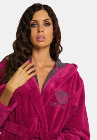 Fuchsia badstof badjas met een grijze capuchon en manchetten, voorzien van een logo op de borst en een bijpassende riem in de taille. Zachte textuur.