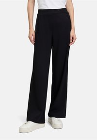 Pantalons larges noirs en tissu doux avec une texture lisse. Possède une taille plate et de subtils accents de poches latérales.