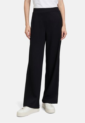 Zwarte wijde broek van zacht materiaal met een gladde textuur. Kenmerkt zich door een platte tailleband en subtiele zijn zakaccenten.