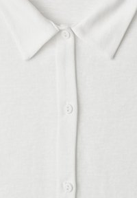 Chemise blanche à col avec trois boutons blancs visibles fermés au centre devant.