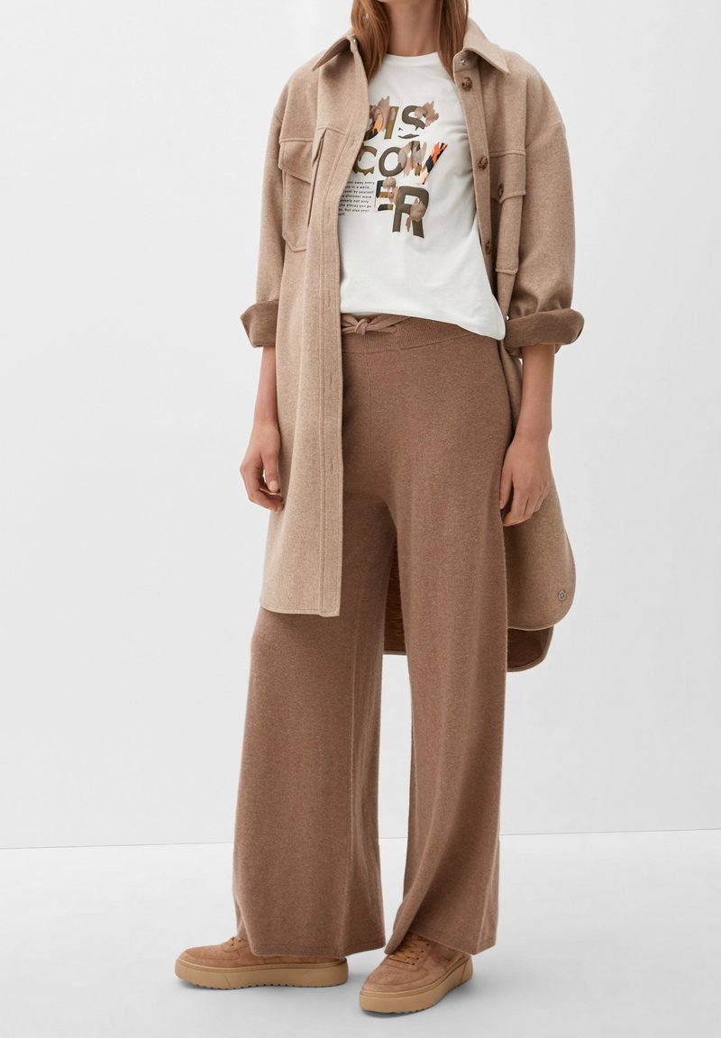 Beige wool blend long shirt, white graphic T-shirt with leaf design, light brown wide-leg pants, and coordinating beige sneakers.