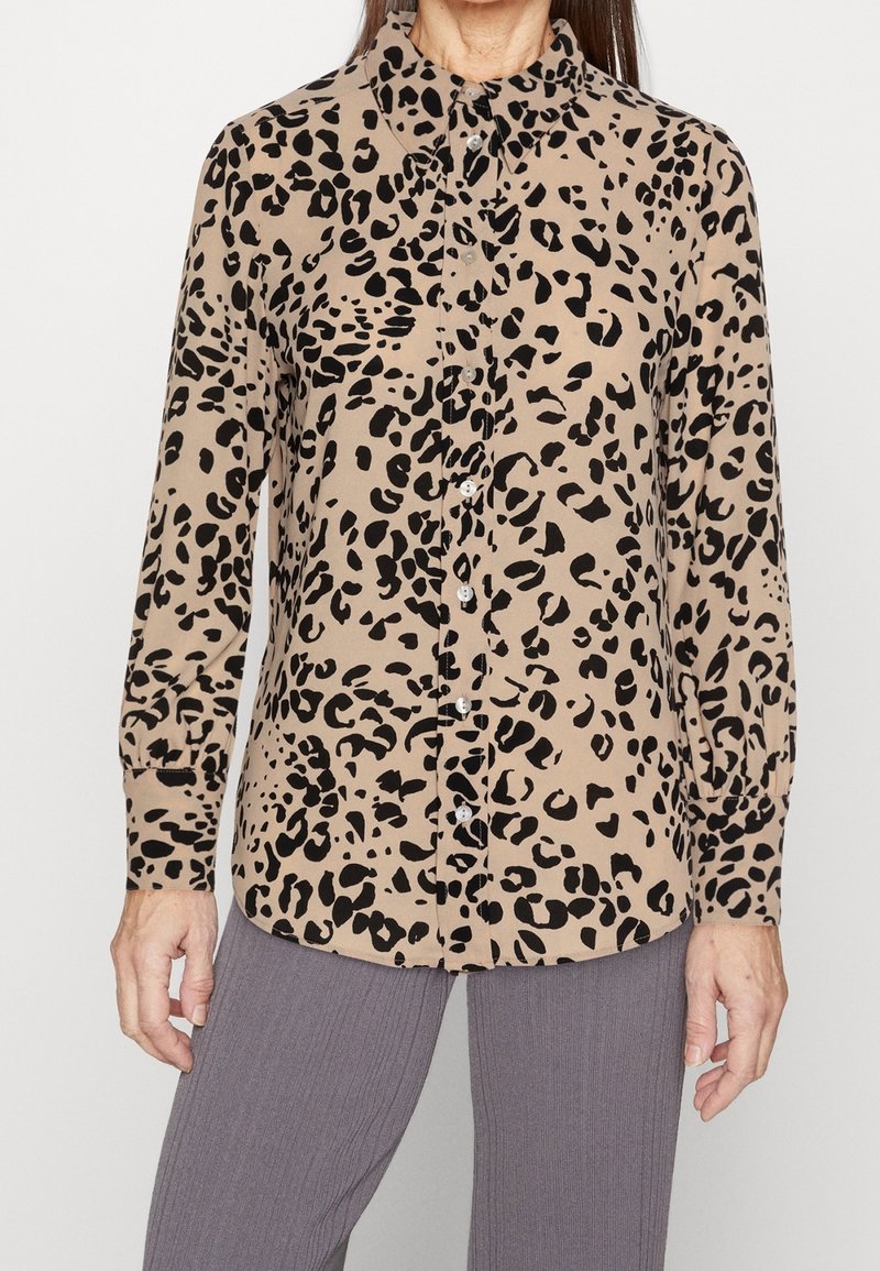 Chemise à boutons imprimé léopard beige à taches noires, avec col, manches longues et texture lisse.