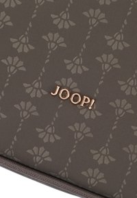 Brunt tygplånbok med ett blommönster i en ljusare nyans, accentuerad med en metallisk "JOOP!"-logotyp i roséguld.