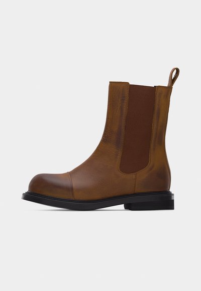 Botte Chelsea en cuir marron avec panneaux latéraux élastiques, semelle noire, bout arrondi et languette à l'arrière.