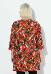 Červené šaty s paisley vzorem a třičtvrtečními rukávy, se černým pozadím, složitými vzory a volným střihem. Měkká textilie.