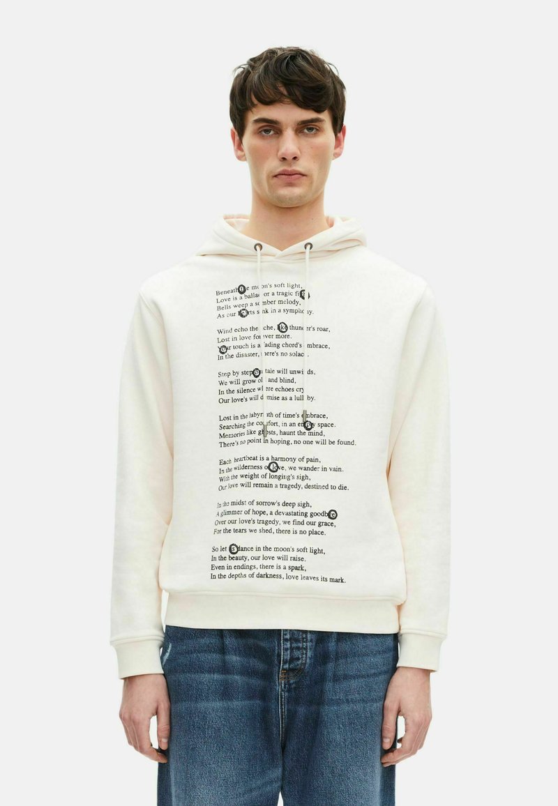 Cremefarbener Hoodie aus weichem Stoff, mit schwarzem Textdesign auf der Vorderseite. Mit Kordelzugkapuze und gerippten Bündchen. Getragen mit hellblauen Jeans.