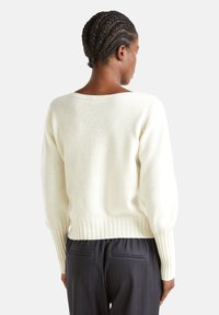 Maglione in maglia color crema con scollo a barca ampio, polsini e orlo rigati, caratterizzato da una vestibilità rilassata. La texture è morbida e dall'aspetto leggero.