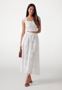 Conjunto de dos piezas blanco de encaje que presenta un top corto con escote cuadrado y mangas cortas, combinado con una falda larga y fluida con una abertura.