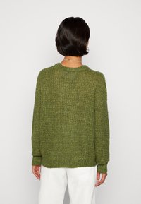 Grön tröja i stickad tyg med lös passform, strukturerad yta, rund halsringning och långa ärmar, kombinerad med vita byxor.