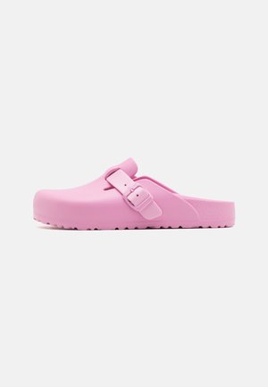 Sabots roses en caoutchouc avec une texture lisse, dotés d'une sangle à boucle sur le côté et d'une semelle épaisse avec un fond à motifs pour une meilleure adhérence.