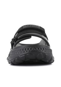 Black slip-on sandal with textured rubber sole and adjustable fabric strap; features logo detailing and distinct arch support.