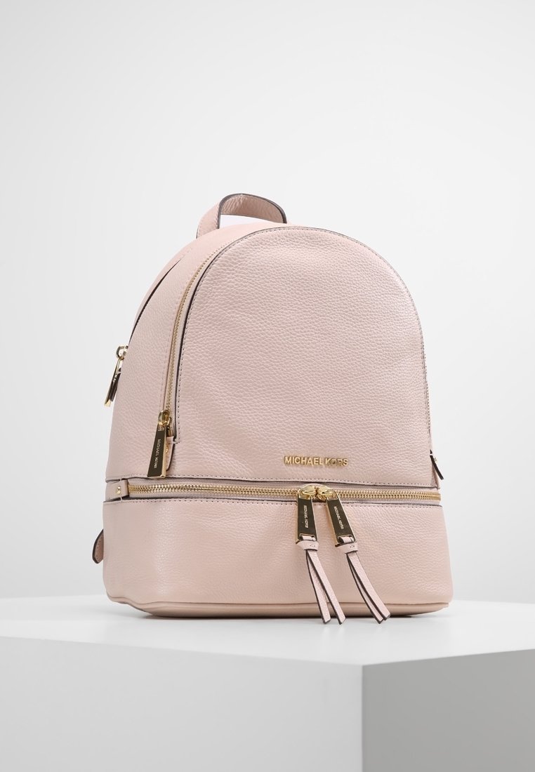 Sac à dos en cuir texturé rose clair avec fermetures éclair dorées et logo Michael Kors, doté de doubles tirettes sur les compartiments avant et principal.