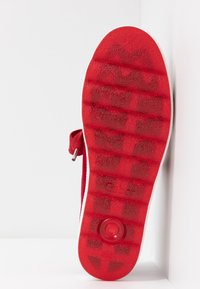 Suela de zapato roja con patrones de agarre texturizados, con un borde blanco y un elemento de diseño circular en el centro. Logotipo del fabricante visible.