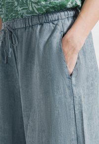 Lichtblauwe linnen broek met een elastische tailleband, trekkoorddetail en zijzakken; gladde textuur, losse pasvorm.