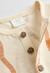 Kortärmad babytopp i krämfärgad med vågiga orange mönster. Har rund halsringning, tre bruna knappar och en märkesetikett.