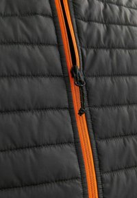 Schwarze gepackte Weste mit einem orangefarbenen Reißverschluss, die eine strukturierte Oberfläche und gepolsterte Bereiche aufweist. Die Reißverschlusszieher sind schwarz und haben eine Schlaufe für einfachen Zugang.