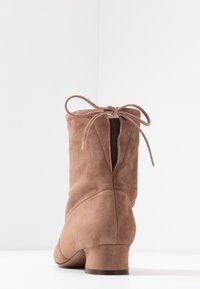 Brun mocka ankelsko med låg klack, med en knytning bak och en slät textur. Enkel design med vertikala sömmar.