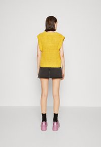 Geel gebreid short-sleeve sweater met een geribbelde textuur, gecombineerd met een zwarte spijkerrok en robuuste roze plateauschoenen.
