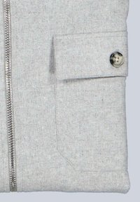 Grau gefütterte Jacke mit strukturiertem Stoff. Verfügt über eine aufgesetzte Tasche mit einem silbernen Knopf und einem glatten Reißverschluss an der Vorderseite.