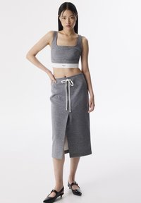 Top grigio corto con spalline larghe e fascia elastica; abbinato a una gonna midi grigia con coulisse e spacco laterale. Scarpe nere con tacco basso.