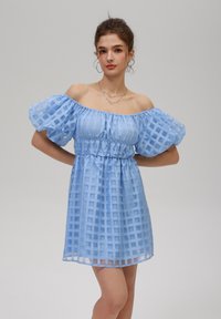 Blårutigt off-shoulder klänning med puffärmar, insvängd midja och en flödande siluett. Lättviktig, genomskinlig tyg med rutmönster.