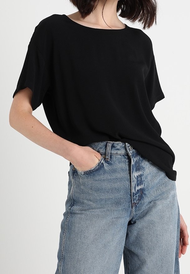 Zwarte losvallende t-shirt met een ronde hals en korte mouwen, gecombineerd met lichtblauwe ripped jeans met hoge taille.