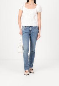 Top bianco con maniche a sbuffo e scollatura quadrata, abbinato a jeans in denim blu. Le calzature presentano un design bicolore, completato da una borsa piccola.