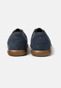 Marinblå mockaskor med en brun gummisula. Mjuk textur, minimalistisk design och en subtil logotypdetalj vid hälen.