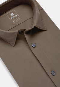 Camicia marrone con colletto caratterizzata da una superficie in tessuto morbido, due bottoni neri e un'etichetta logo visibile all'interno del colletto.