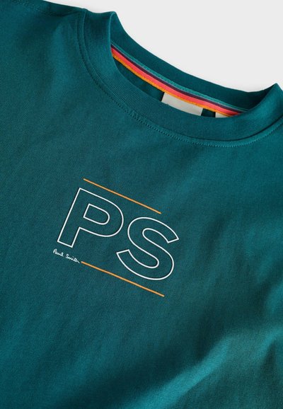 Turkosa bomullströja med en vit och orange "PS"-logotyp, rund halsringning och flerfärgade randiga detaljer vid kragen.