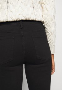 Jeans de denim negro con un diseño de cintura alta, con bolsillos traseros y una textura suave, combinados con un suéter de punto crema.