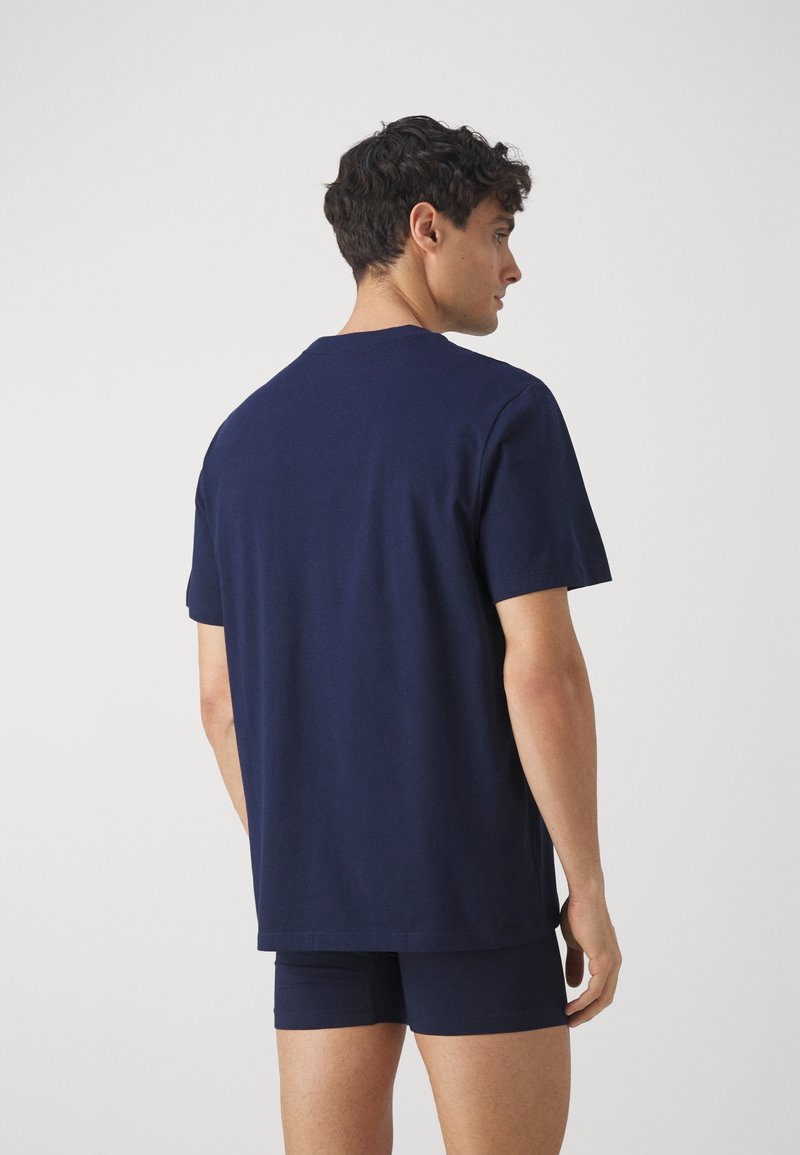 T-shirt in cotone blu navy con maniche corte, vestibilità rilassata, scollatura rotonda, texture morbida, indossato con pantaloni shorts abbinati, visto da dietro.