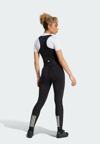 Zwarte sportieve jumpsuit met witte korte mouwen, nauwsluitend ontwerp, getextureerde stof en drie witte strepen op de benen. Achteraanzicht.