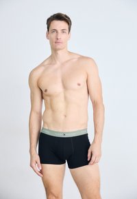 Sorte boxer briefs med en lys grøn elastik med "TOMMY HILFIGER" logoet. Stoffet ser glat og tætsiddende ud.