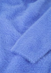 Zacht, pluizig lichtblauw stof met fijne vezels en een opgevouwen mouwdetail zichtbaar op een vlakke ondergrond.