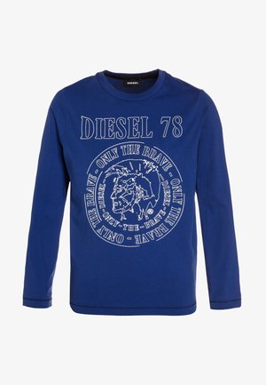 Blå langærmet skjorte med teksten "DIESEL 78" og et cirkulært logo med et stiliseret mandligt ansigt og teksten "ONLY THE BRAVE" gentaget rundt om.
