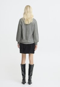 Maglione grigio lavorato a maglia con design a coste e maniche a sbuffo; indossato con una gonna in corduroy nera e stivali neri sopra il ginocchio.