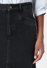 Črna jeans krilo z visokim pasom, ki ima sprednje gumb in zadrgo, stranske žepe ter gladko, teksturirano površino.