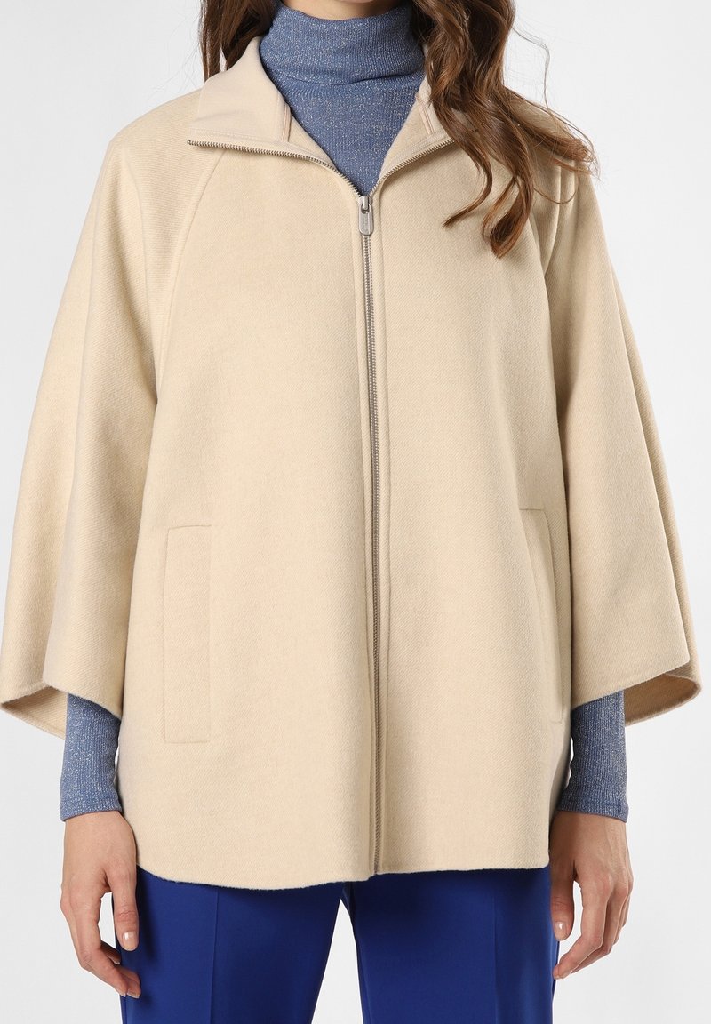 Beige zip-up kappejakke med rund krave, løse ærmer og to frontlommer. Lavet af blødt stof, som fremviser en glat tekstur.