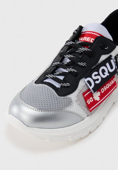 Αθλητικό παπούτσι από δίχτυ με μαύρο και ασημί εξωτερικό, με έντονο κόκκινο και μπλε λογότυπο. Υφή φινιρίσματος και αντίθετα μαύρα κορδόνια.