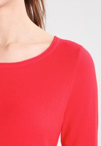 Chemise rouge à manches longues en tissu doux et côtelé. Dotée d'un col rond et d'une coupe ajustée, mettant en valeur une texture lisse et une couleur vive.