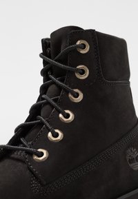 Černé sukované boty na tkaničky s kovovými očky a strukturovanými koženými akcenty. Mají silné černé tkaničky a logo vyražené na boku.