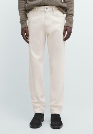 Pantaloni beige in cotone con design a gamba dritta, dotati di tasche frontali, chiusura con bottone e cerniera, indossati con scarpe nere in camoscio.