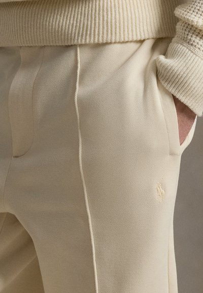 Κρεμ παντελόνια από υφασμάτινο ύφασμα με υφή, με πλαϊνές τσέπες και κεντημένο λογότυπο. Διακοσμημένα με διακριτικές λεπτομέρειες ραφής.