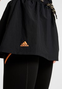 Svart Adidas-kjol med orange logotyp som bärs över svarta leggings med orangea detaljer och synlig dragsko i midjan.