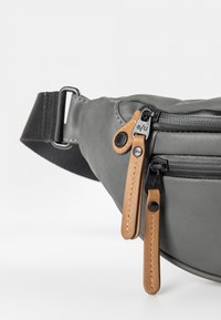 Sac banane en tissu gris avec des zips noirs et des tirettes en cuir tan. Dispose d'une sangle ajustable et de détails de couture subtils.