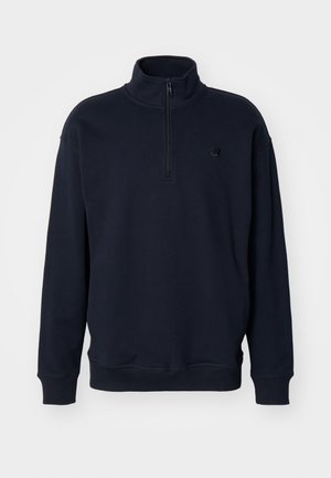 Sweatshirt pulover bleu marin cu guler înalt, fermoar la gât și un design ajustat al manșetelor. Prezintă un logo subtil pe piept.