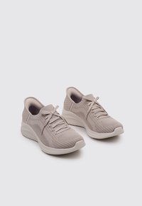 Scarpe da ginnastica di un beige chiaro con tomaia in maglia, chiusura con lacci, colletto imbottito e suola texturizzata per aderenza e comfort.